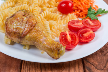 Fried chicken leg against cooked spiral pasta, vegetables, close-up
