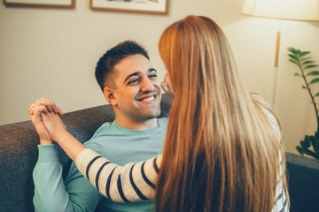 Fototapeta premium Young man laughing while having fun at couch at home with her girlfriend which is sitting on him.