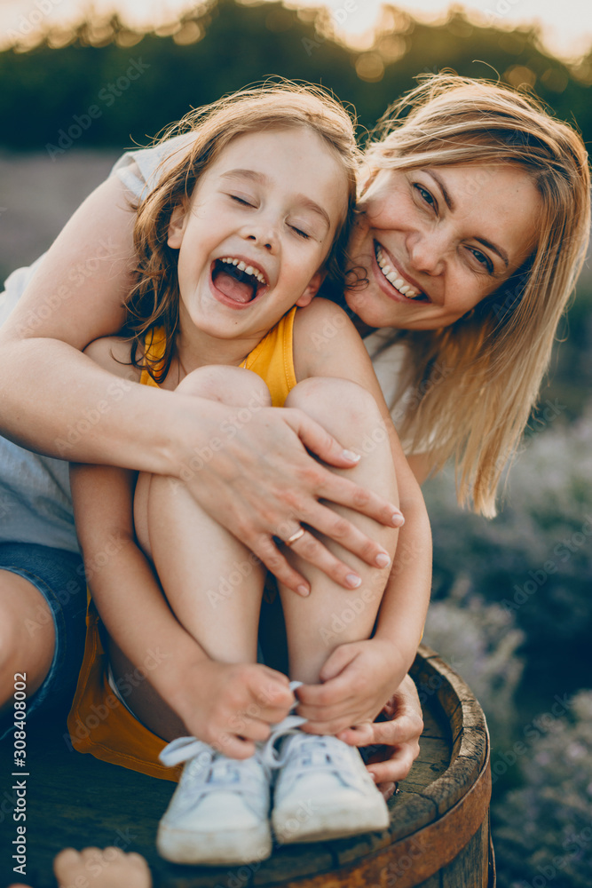 Wall mural portrait of a lovely little girl laughing with closed eyes while is embraced by her mother with is l