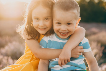 Close up of a cute little brother and sister embracing and looking at camera laughing while sitting...