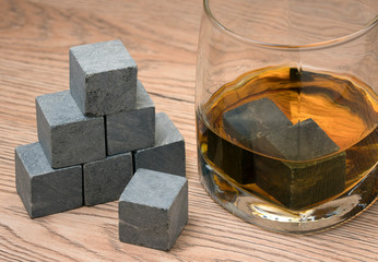 Stones in glass of whiskey on wooden background.
