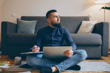 Full length portrait of a confident male freelancer sitting on the floor looking away while holding...