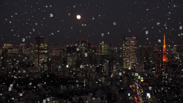 TOKYO, JAPAN - DECEMBER 2019 : Aerial view of cityscape of TOKYO snowing at night. Scenery of central downtown area. Soft snow falling and full moon in the sky. Winter and Christmas season concept.