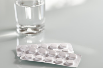 Still life with two blister packs with antibiotic tablets and a glass of water on  white background