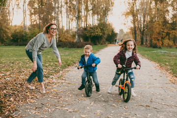 Lovely little brother competing with his sister riding bicycles outdoor in the park while their mother is giving them start.