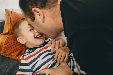 Close up portrait of a lovely little son playing with his father in the morning in the bed at their home.