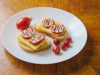 Simple home made sandwich with bread, red cheddar cheese, and decorated with mayo and herbs on a white plate and wooden table.