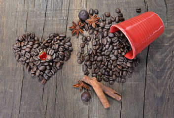 heart shaped jewel  in beans of coffee forming a heart next to a spilled red cup full of beans on wooden background
