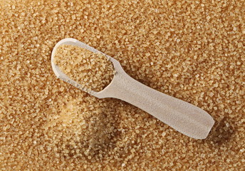 Brown cane sugar crystals with wooden spoon background and texture