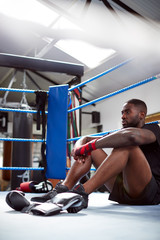 Tired Male Boxer Sitting In Boxing Ring In Gym After Training Session