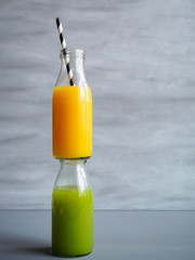 Orangensaft und grüner Gemüsesaft gestapelt in einer Glasflasche auf einem grauen Hintergrund, gesunde Ernährung, Abnehmen