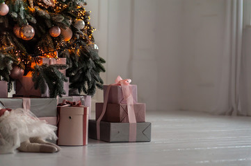 Gifts boxes under decorated Christmas tree in white interior, background