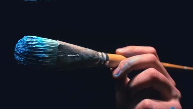 The artist draw on glass. Back view. Craftsman decorator use large brush and blue acrylic oil paint. Indoor. Dark magic cinematic look, black background. Artist Brush draw directly on glass screen.