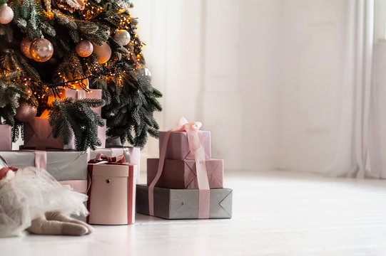 Gifts boxes under decorated Christmas tree in white interior, background