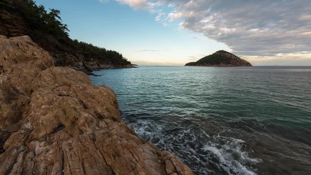 Time lapse with sunset at the rocky coastline of Thasos island and view to little island Nisida Kinira, Greece