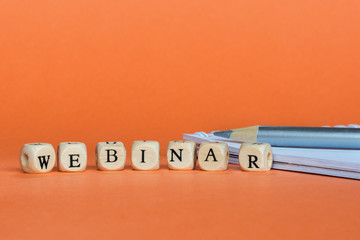 Concept webinar (online workshop, training, internet learning, teaching seminar education)  Wooden Blocks with the text: Webinar.  notebook and pencil. Orange background, copy space - 308416032