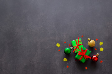 Gifts in green paper with red and yellow ribbons, gold, red and green christmas balls and confetti in the form of red stars are on the right. Black background, copy space. Big sale concept