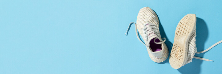 White sneakers under morning sunlight on a blue background.Jogging, running, fitness, cross fit, hard workout. Morning run. Banner. Flat lay, top view