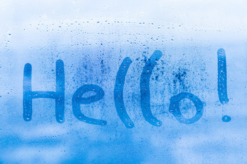 The child inscription hello on the blue evening or morning window glass with drops 