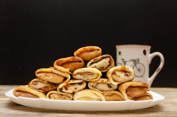 Homemade pancakes with filling stacked in a pyramid on a white plate against a black wall with a Cup, copy space