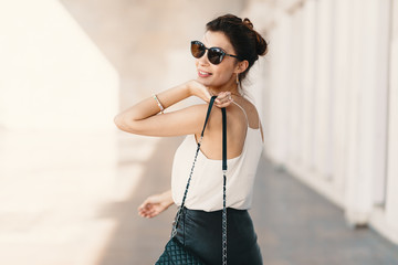 Beautiful smiling young woman in sunglasses looking away over the shoulder while walking