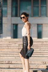 Fashionable brunette businesswoman in leather pencil skirt and sunglasses walking on stairs