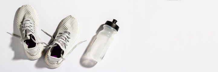 White sneakers and a bottle with water under morning sunlight on a white background. Concept,...