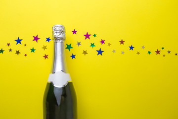 Champagne bottle with colorful glittering stars holiday abstract on yellow.