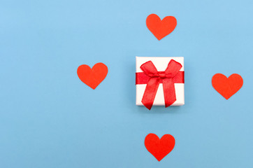 Gift box among red paper hearts on a blue background. Top view, copy space. Valentine's day, a symbol of love. Festive background