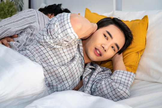 Asian Homosexual Couple In Pajamas Snoring And Bad Sleeping On The Bedroom.He Blocking Ears With Hands.Concept LGBT Gay.