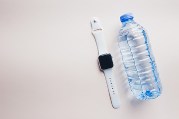 Top view of sport accessories and equipment for fitness and running. Fitness bracelet or watch and water isolated on pink background.