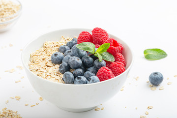 Breakfast smoothie bowl with granola, fresh raspberries, blueberries and mint on white background. Healthy food.