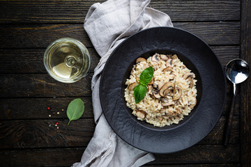 Risotto with mushrooms in a black plate over rustic wooden background, top view