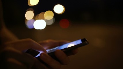 Fingers touching smartphone screen with bokeh of headlights passingby cars