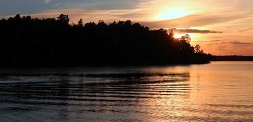 Fototapeta premium glowing evening sun behind the forest on a fjord
