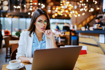 Focused attractive fashionable shopaholic sitting in cafe and searching online for things she want to buy. Next to her on chair are shopping bags.