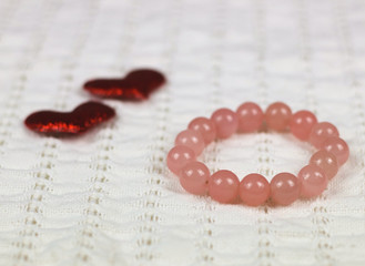Rose quartz bracelet on white cloth with two red glitter hearts.