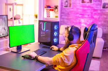 Man playing on powerfull gaming pc in a room with neon lights on a green screen computer © DC Studio