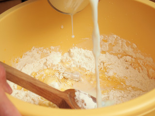 Pouring milk into bowl with batter. Making yeast pancakes (crepes).