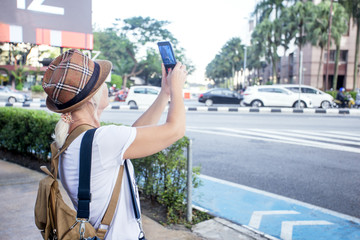 Woman blogger taking photo with her smartphone in Kuala-Lumpur. Travel in Asia concept. Blogging.
