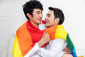 Obraz premium Portrait of Asian homosexual couple hug and holding hand with pride flag in bedroom.Concept LGBT gay.