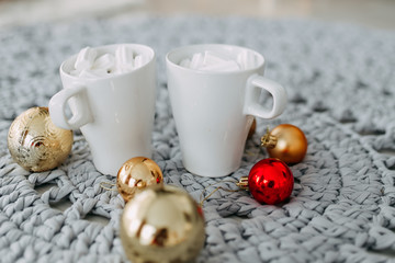 Beautiful Christmas picture. Two white cups of coffee with marshmallow and a few Christmas tree colored balls of toys lie on a delicate textured background.