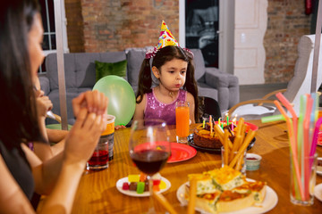 Mother and daughter celebrating a birthday at home. Big family eating cake and drinking wine while greeting and having fun children. Celebration, family, party, home, childhood, parenthood concept.