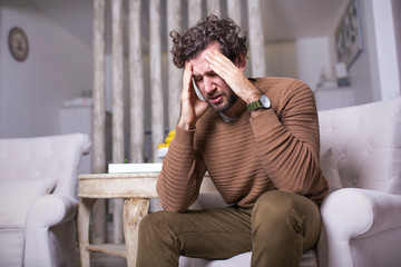 Portrait of an handsome man sitting on a sofa at home with a headache, feeling pain and with an...