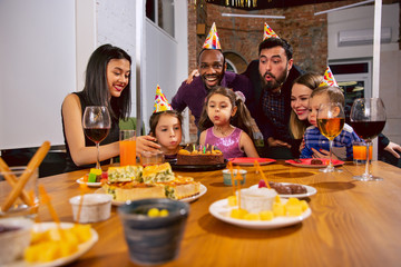 Portrait of happy multiethnic family celebrating a birthday at home. Big family eating snacks and drinking wine while greeting and having fun children. Celebration, family, party, home concept.
