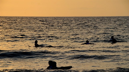 Documentation of surfers in action at dusk with a golden color and dark, unfocused and dark on the beach of Senggigi Lombok, West Nusa Tenggara Indonesia, 27 November 2019