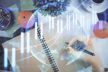 Forex chart hologram on hand taking notes background. Concept of analysis. Double exposure