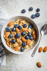 Healthy quinoa porridge with blueberries and almonds with syrup in gray bowl, top view. Vegan food concept.