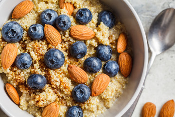 Healthy quinoa porridge with blueberries and almonds with syrup in gray bowl, top view. Vegan food concept.