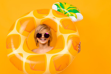 portrait of a smiling european blond boy in yellow swimming trunks and sunglasses with a swimming circle pineapple on an orange background